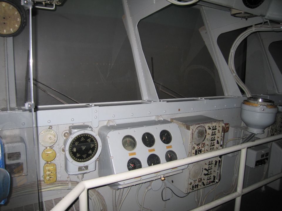 Ship bridge interior showing gray instrument panels, gauges, gyrocompass and windows