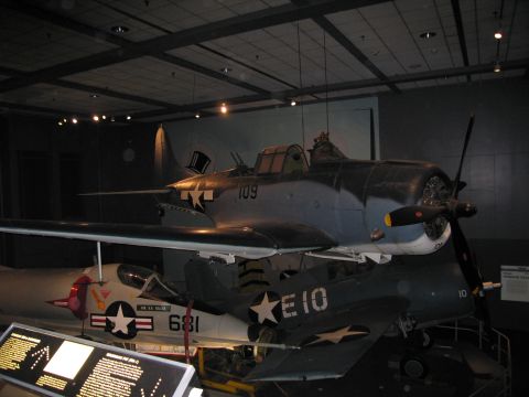 1991 Ford LTD Crown Victoria - gray WWII-era Navy aircraft marked 109 displayed above a silver jet with code E10 and number 681 in a museum.