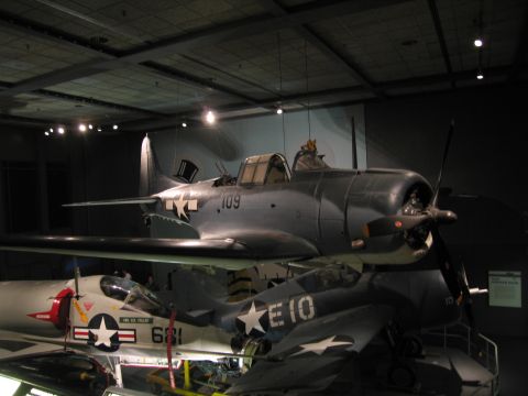 1991 Ford LTD Crown Victoria - gray WWII-era Navy aircraft marked 109 with a propeller, shown above other aircraft including code E10 in a museum.
