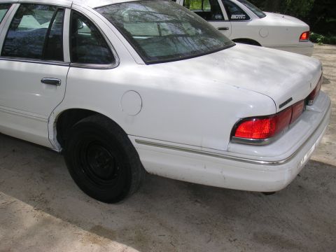 1997 Ford Crown Victoria - Two white sedans are parked outdoors, one in front of the other. The rear of the closest car is visible.