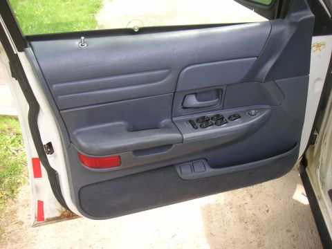 1997 Ford Crown Victoria - Interior of a car door panel, showing gray upholstery and controls. The door jamb exhibits water stains.