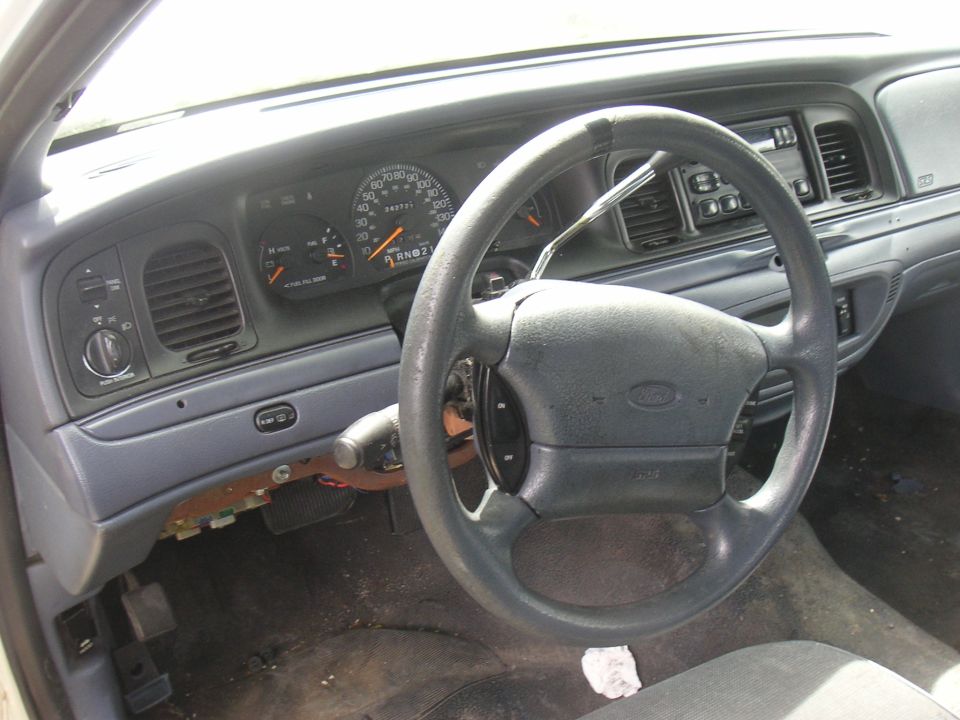 Gray Ford sedan dashboard and steering wheel with lower trim removed exposing wiring