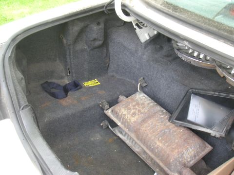 1997 Ford Crown Victoria - Car trunk contains a muffler, cloth item, and hubcap; yellow sticker present.