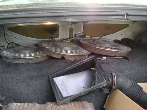 1997 Ford Crown Victoria - The trunk of a car contains several hubcaps and parts of an air intake system.