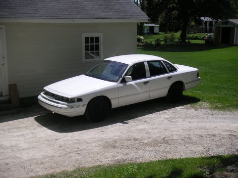 1997 Ford Crown Victoria - A white sedan sits in a driveway next to a house, appearing to be a project car.