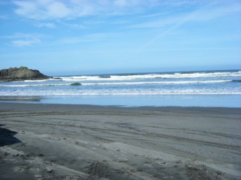2005 Jeep Wrangler - Tire tracks mark the sand on a beach, leading towards the ocean waves under a bright blue sky.