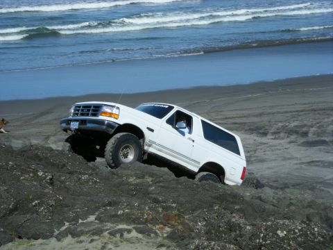 2005 Jeep Wrangler - White Ford Bronco driving on a rocky beach with waves in the background.