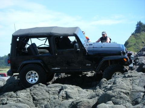 2005 Jeep Wrangler - Black Jeep Wrangler on rocky terrain, likely off-roading near the coast.