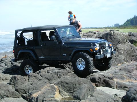 2005 Jeep Wrangler - A black Jeep Wrangler navigates rocky terrain by the sea under a clear sky.