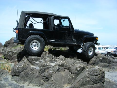 2005 Jeep Wrangler - A black Jeep Wrangler navigates a rocky terrain near the coast.