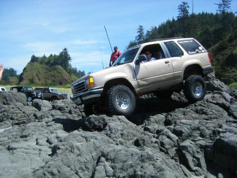 2005 Jeep Wrangler - Ford Explorer navigates rocky terrain near the coast, with other vehicles in the background.