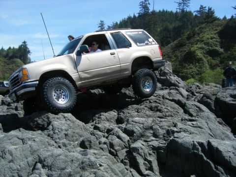 2005 Jeep Wrangler - A modified Ford Explorer navigates a rocky coastal terrain under a clear blue sky.