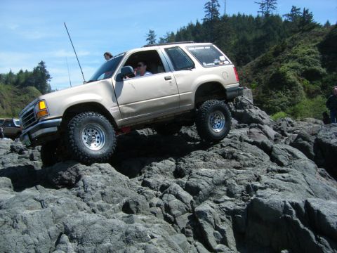 2005 Jeep Wrangler - A tan SUV is shown off-roading over large rocks on a sunny day.