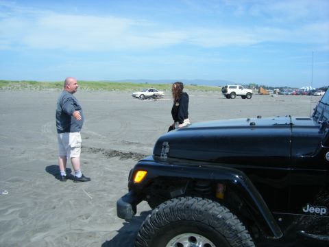 2005 Jeep Wrangler - A black Jeep Wrangler is parked on a sandy beach with people and other vehicles in the background under a partly cloudy sky.