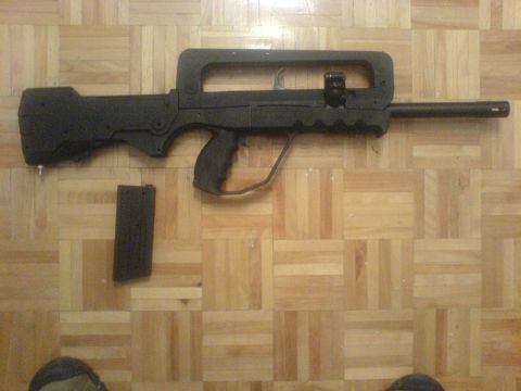 1985 Ford Bronco - A black rifle with its magazine lies on a parquet wood floor. The SuperMotors logo is visible in the lower right corner.