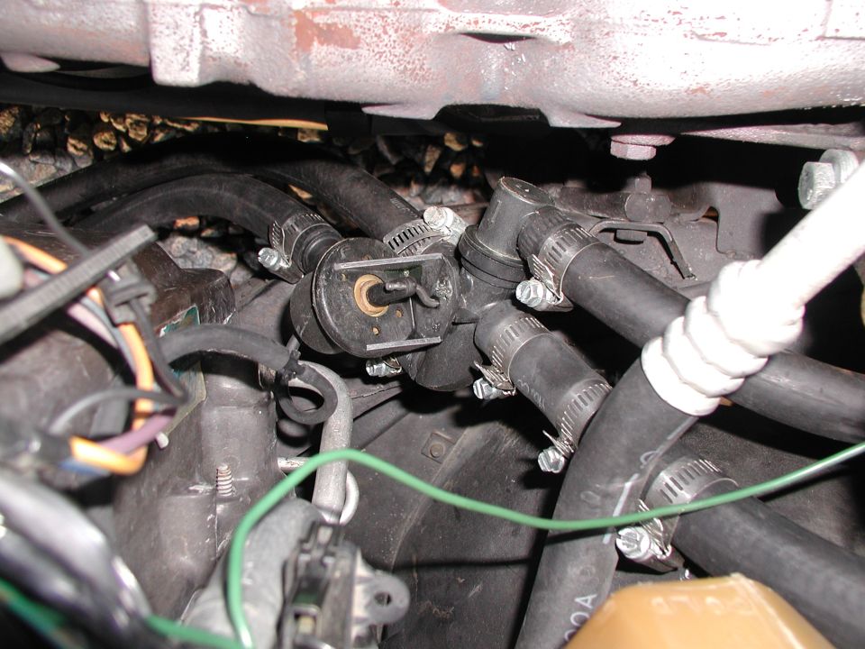 Engine bay close-up of hoses, clamps, and a sensor with a green wire