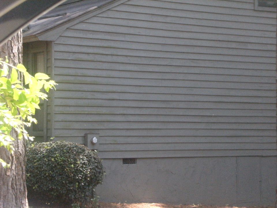 Side view of a gray building with horizontal siding and a green bush