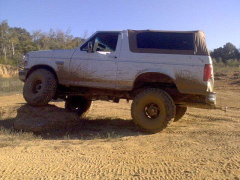 1996 Ford Bronco - A muddy white Ford Bronco navigates an off-road course under a clear blue sky.