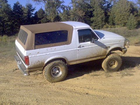 1996 Ford Bronco - This lifted Ford Bronco navigates an off-road trail, its white body covered in mud.