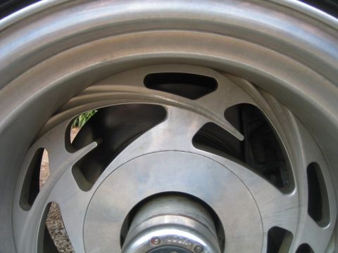 1996 Ford Bronco - Tight close-up of a polished aluminum slotted mag wheel with teardrop-shaped vent slots and a lipped outer rim, mounted on a vehicle. The b…