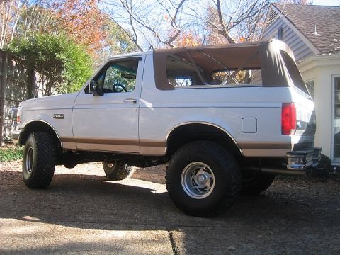 1996 Ford Bronco - White Ford Bronco with tan two-tone lower trim fitted with a tan soft top in place of the hardtop, its rear curtain partly folded open. See…