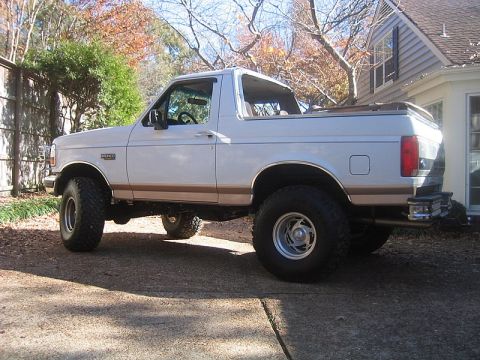 1996 Ford Bronco - White Ford Bronco with tan lower two-tone and Eddie Bauer-style trim, shot in profile in a residential driveway with its rear top removed a…