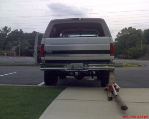 1996 Ford Bronco - Straight-on rear view of a lifted white and tan Ford SUV with its rear glass raised and driver's door open, showing the chrome rear bumper,…