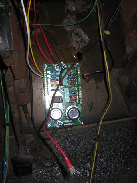 1979 Ford Bronco - A close-up view of a wiring harness and fuse block mounted under the dashboard of a vehicle. The fuse block has labels for various electric…