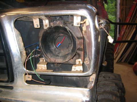 1979 Ford Bronco - Close-up view of the headlight assembly area of a vehicle, showing exposed wiring and a black headlight housing. The chrome bumper and part…