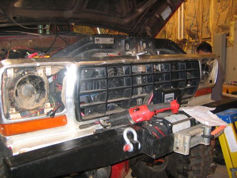 1979 Ford Bronco - A close-up view of the front grille and headlight area of a red vehicle, likely a Ford Bronco, undergoing work. A red power tool rests on a…