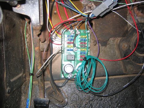 1979 Ford Bronco - A close-up view of a custom wiring harness and fuse block installed under the dashboard of a vehicle. The fuse block has multiple labeled f…