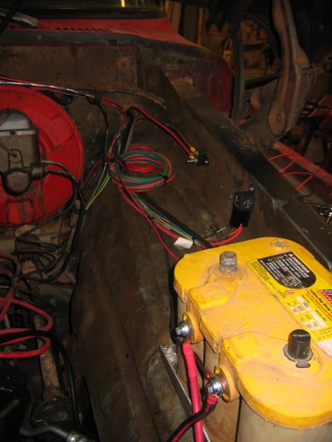 1979 Ford Bronco - Wiring harness and battery in a vehicle's engine bay. The battery is yellow and has red and black cables attached.