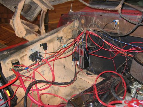 1979 Ford Bronco - The engine bay of a red vehicle, likely a Ford Bronco, is filled with a complex wiring harness, a black electronic control unit labeled "Of…