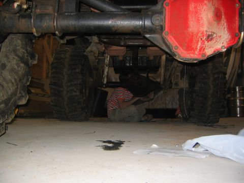 1979 Ford Bronco - A person is working underneath the rear differential of a large off-road vehicle, possibly a Ford Bronco, with large tires and a red differ…