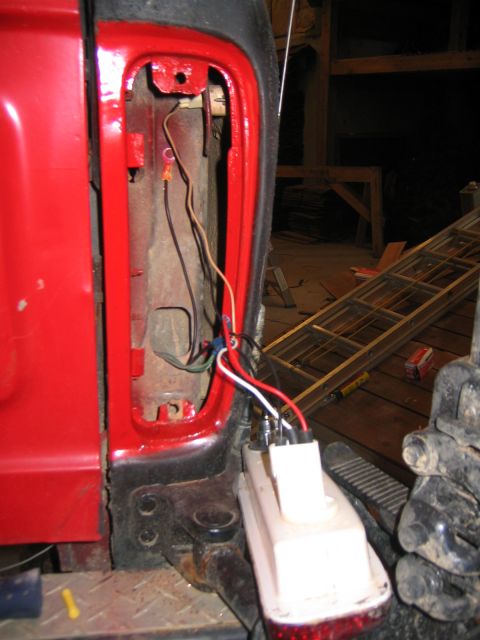 1979 Ford Bronco - Close-up view of the wiring harness being connected to the taillight assembly of a red vehicle. The taillight housing is removed, revealing…