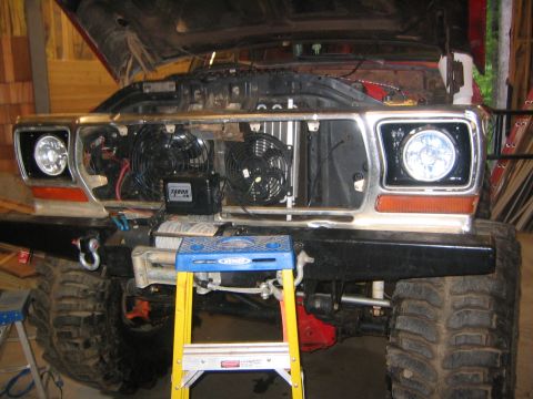 1979 Ford Bronco - The front end of a red 1979 Ford Bronco is shown with its hood open, revealing the engine bay and two electric fans. A winch and a blue ste…