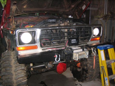1979 Ford Bronco - The front end of a red off-road vehicle with its hood open shows a large winch mounted on the custom bumper. The vehicle has large, aggress…