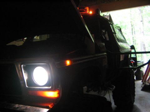 1979 Ford Bronco - The front driver's side headlight of a dark-colored vehicle is illuminated, with orange turn signals visible above and below it. The vehicl…