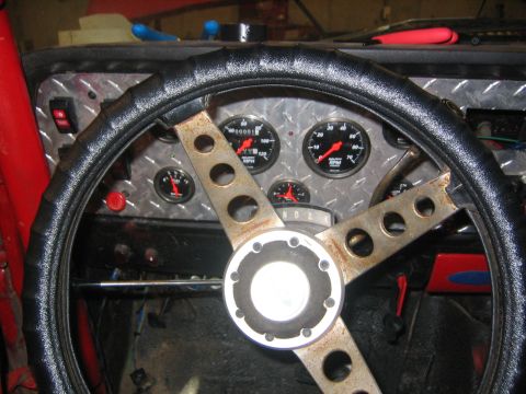 1979 Ford Bronco - The interior of a vehicle shows a close-up of a custom steering wheel with a diamond plate dashboard and multiple gauges. A red button and…