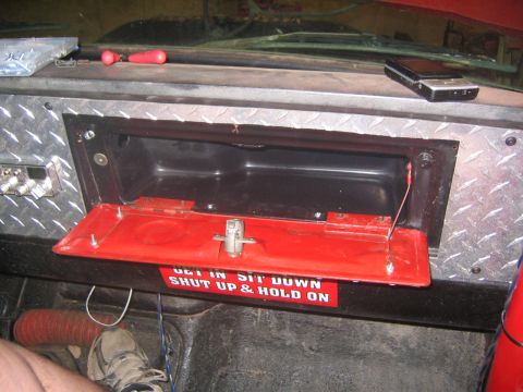 1979 Ford Bronco - The interior of a vehicle shows an open red glove box with a warning sticker that reads "GET IN, SIT DOWN, SHUT UP & HOLD ON". A cell phone…