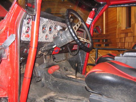 1979 Ford Bronco - The interior of a modified red off-road vehicle, likely a 1979 Ford Bronco, shows a custom dashboard with gauges, a roll cage, and racing s…