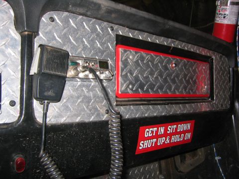 1979 Ford Bronco - A close-up view of the dashboard of a vehicle, featuring a CB radio with a microphone and a red and white sticker that reads "GET IN SIT DO…