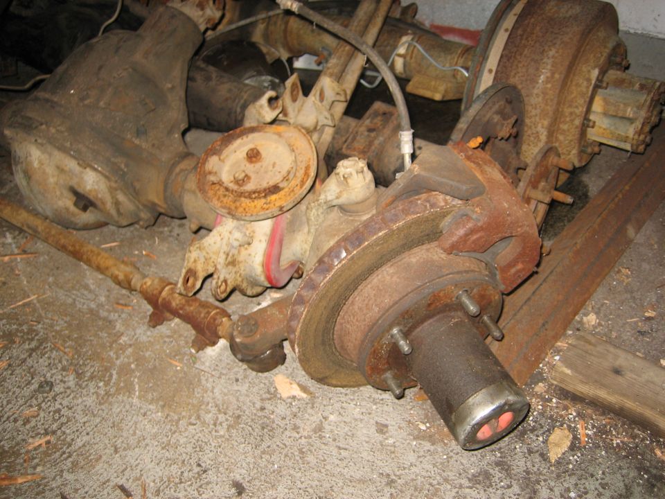 Rusty truck/SUV axle and brake assemblies piled on concrete floor.