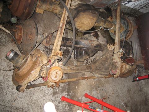 1990 Ford Bronco - This image shows a collection of heavily rusted vehicle axle assemblies and brake components, likely from a 1990 Ford Bronco, stored on a c…