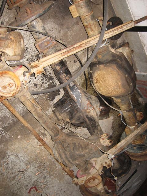 1990 Ford Bronco - A collection of rusty, old Ford Bronco rear axle assemblies and related suspension components are piled on a concrete floor. The parts are…