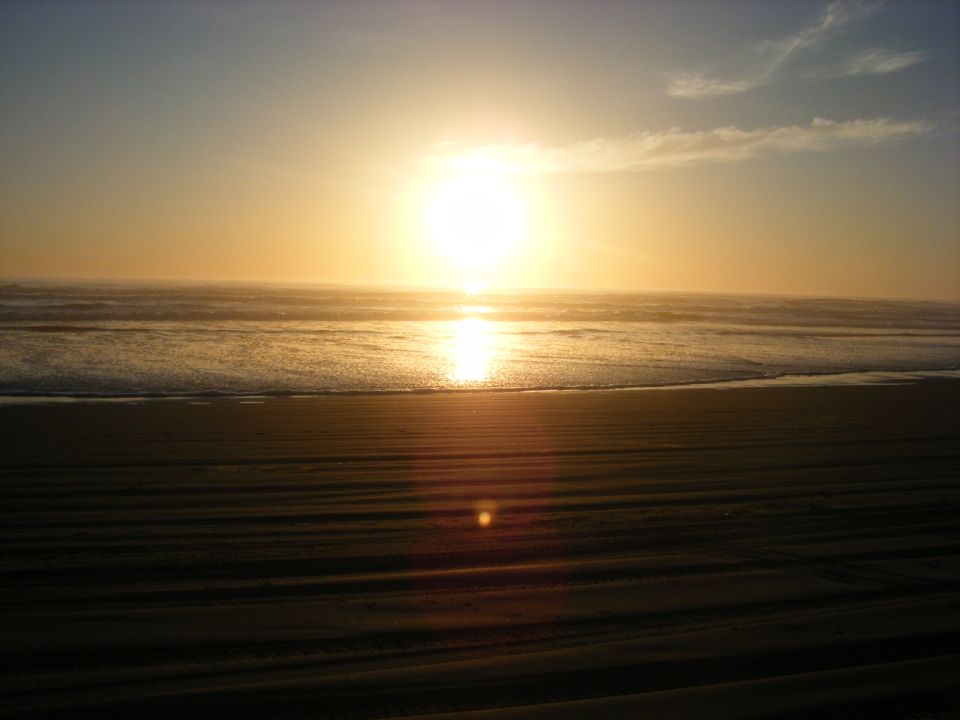 Sunset over the ocean with waves and a sandy beach.
