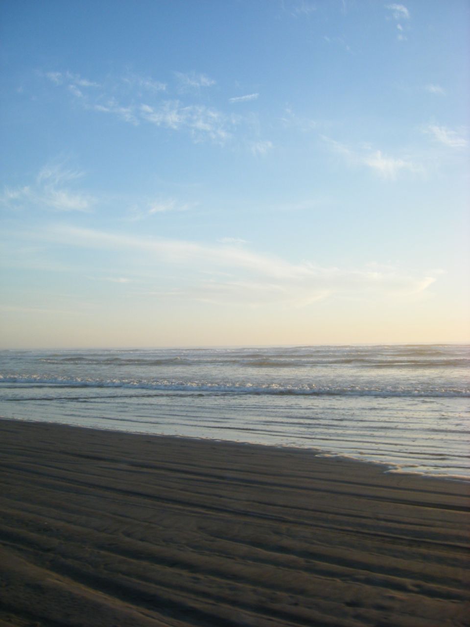 Beach scene with waves and sand under a cloudy sky.