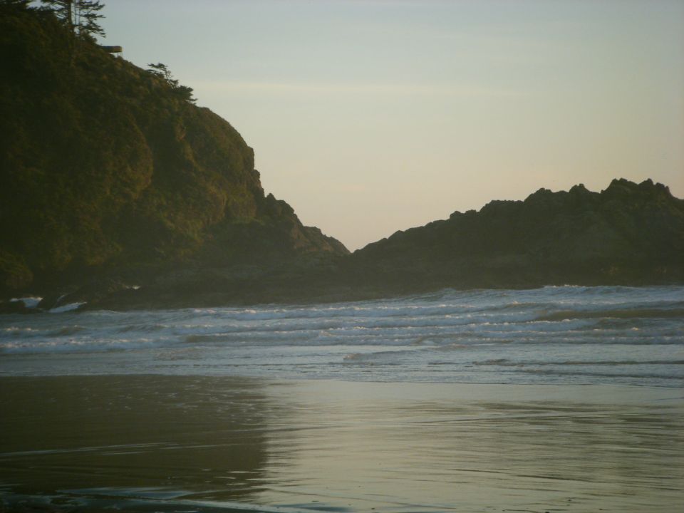 Rocky coastline with waves and a hazy sunset.