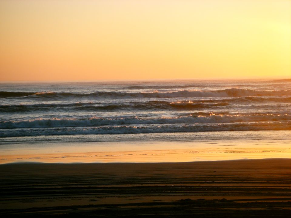 Sunset over the ocean with waves crashing on the beach.