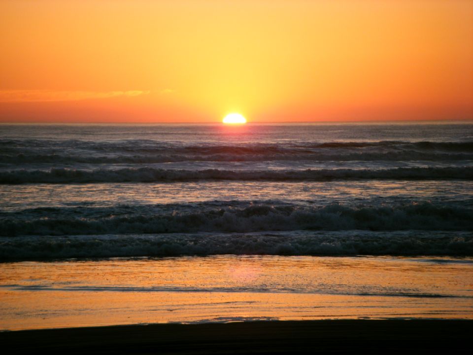 Sunset over the ocean with waves and reflections on the sand.